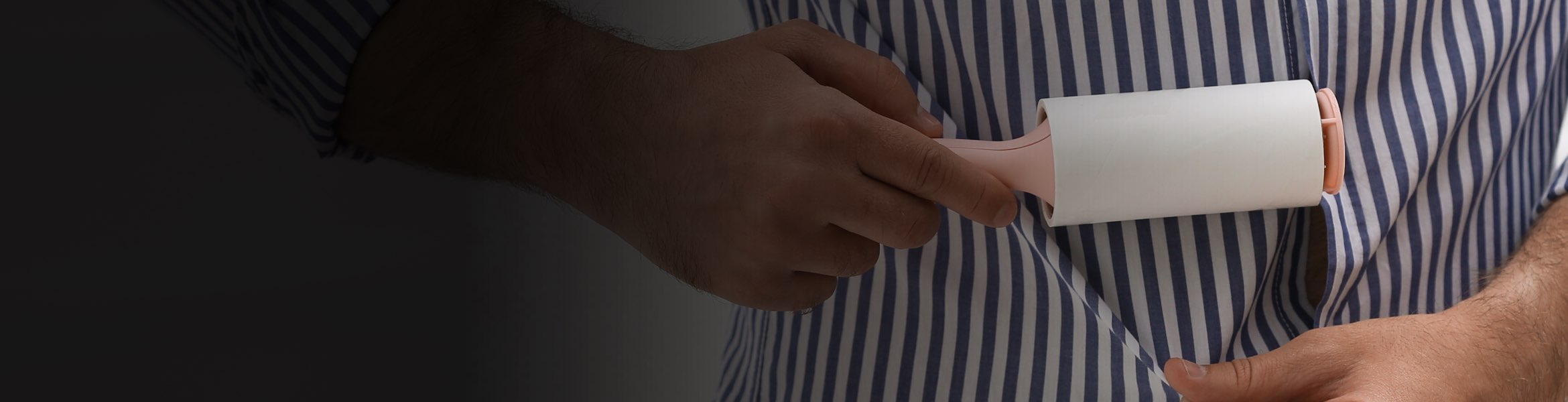 A person in a blue and white striped shirt pulls their shirt down to remove lint with a lint roller