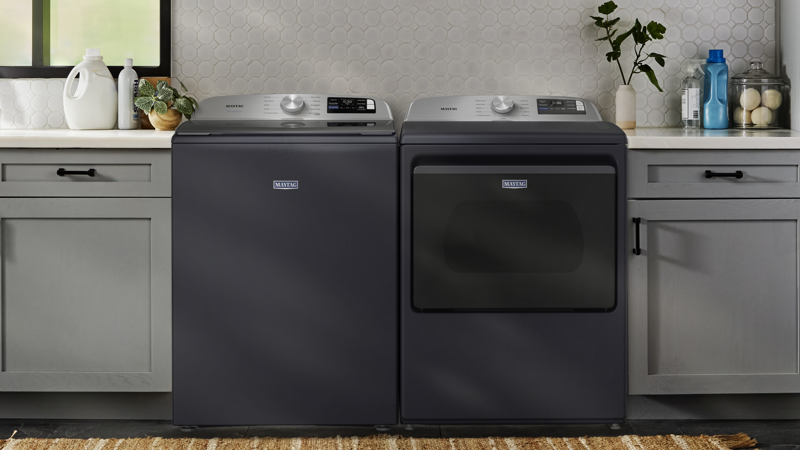  Maytag® top load washer and dryer in between gray cabinetry in a laundry room