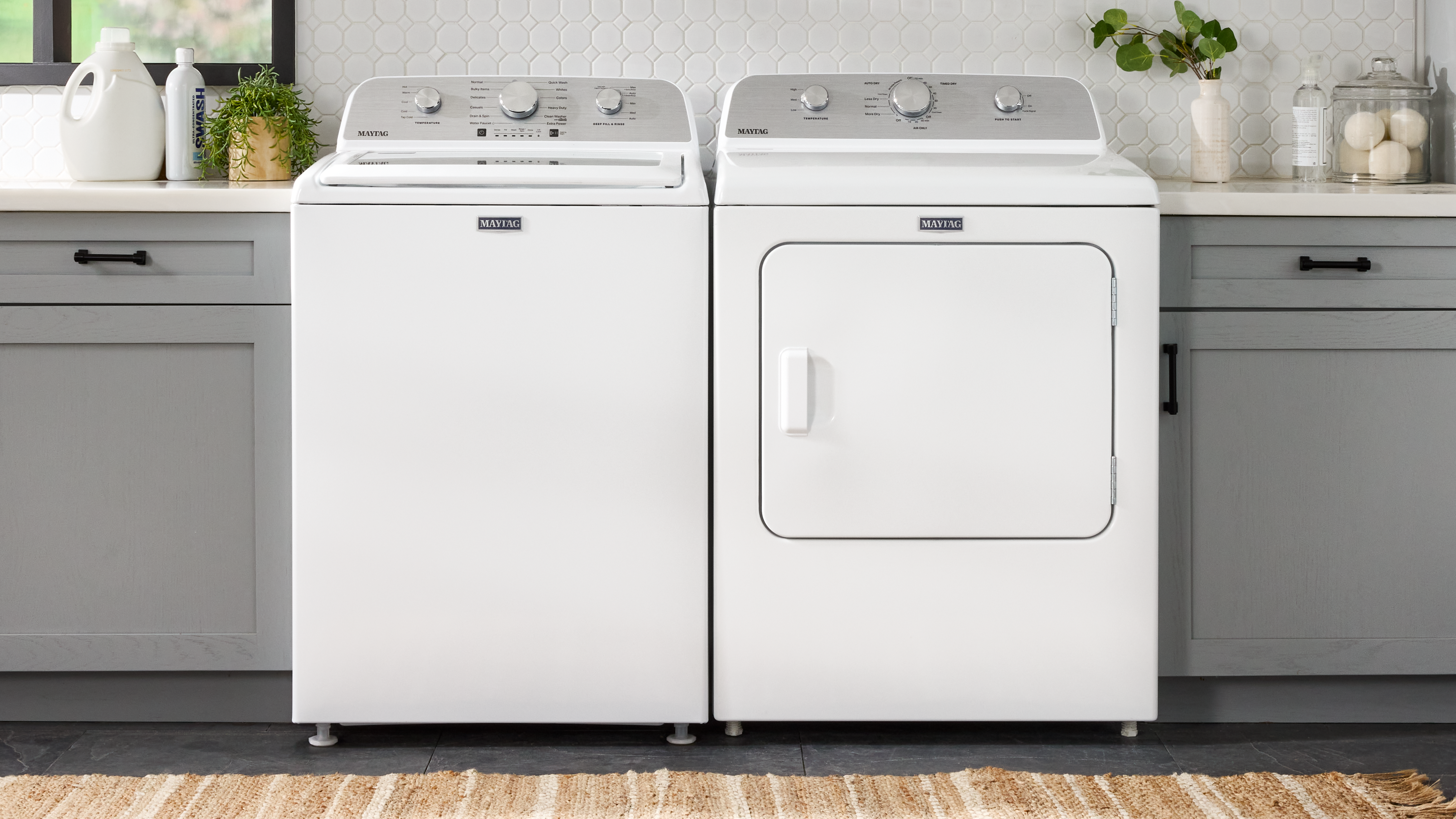  A white Maytag® top load washer and dryer next to grey cabinetry
