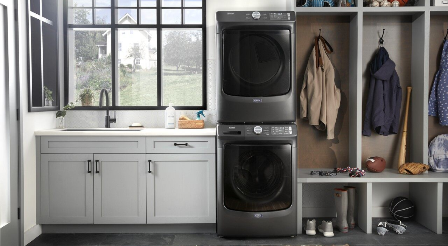 Stacked Maytag® front load laundry pair next to shelving in laundry room