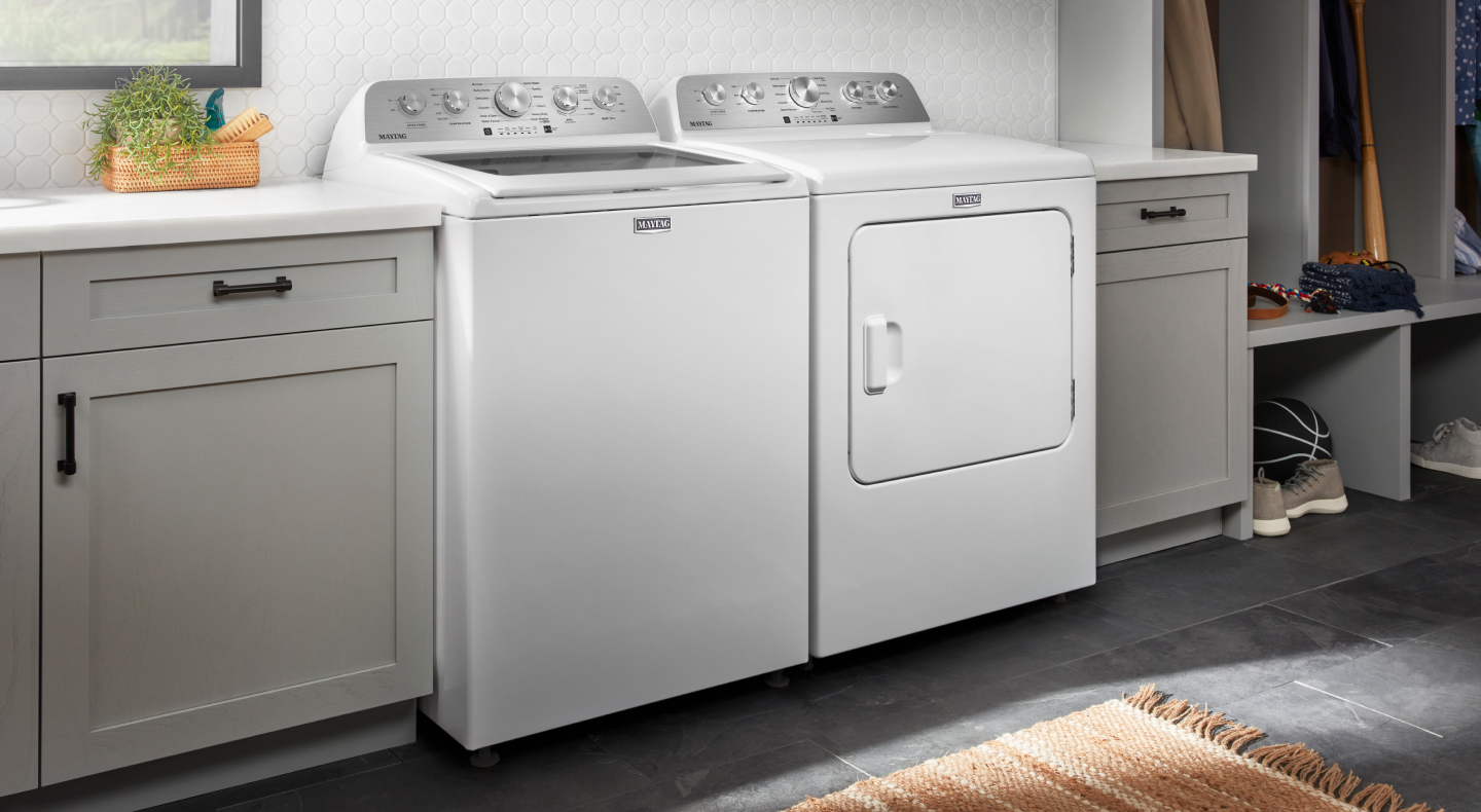 White Maytag® top load washer and dryer pair between gray cabinets