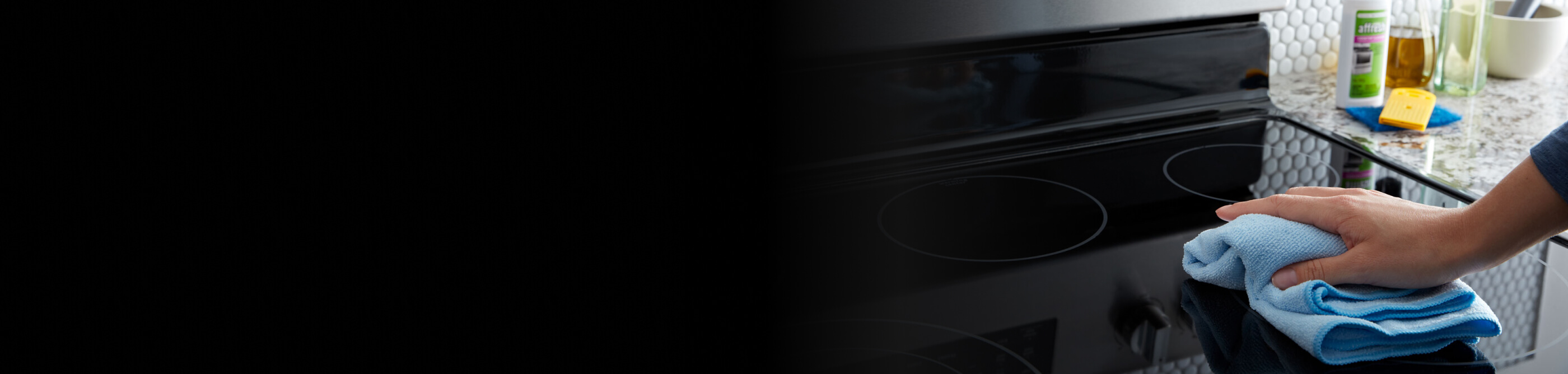 Person wiping down a glass Maytag® cooktop