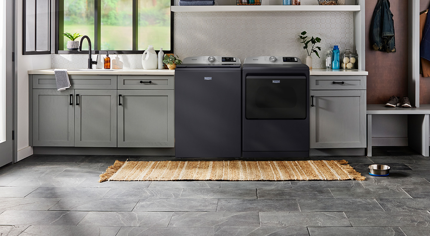 Midnight Steel Maytag® top load washer and dryer pair between cabinets in a laundry room 