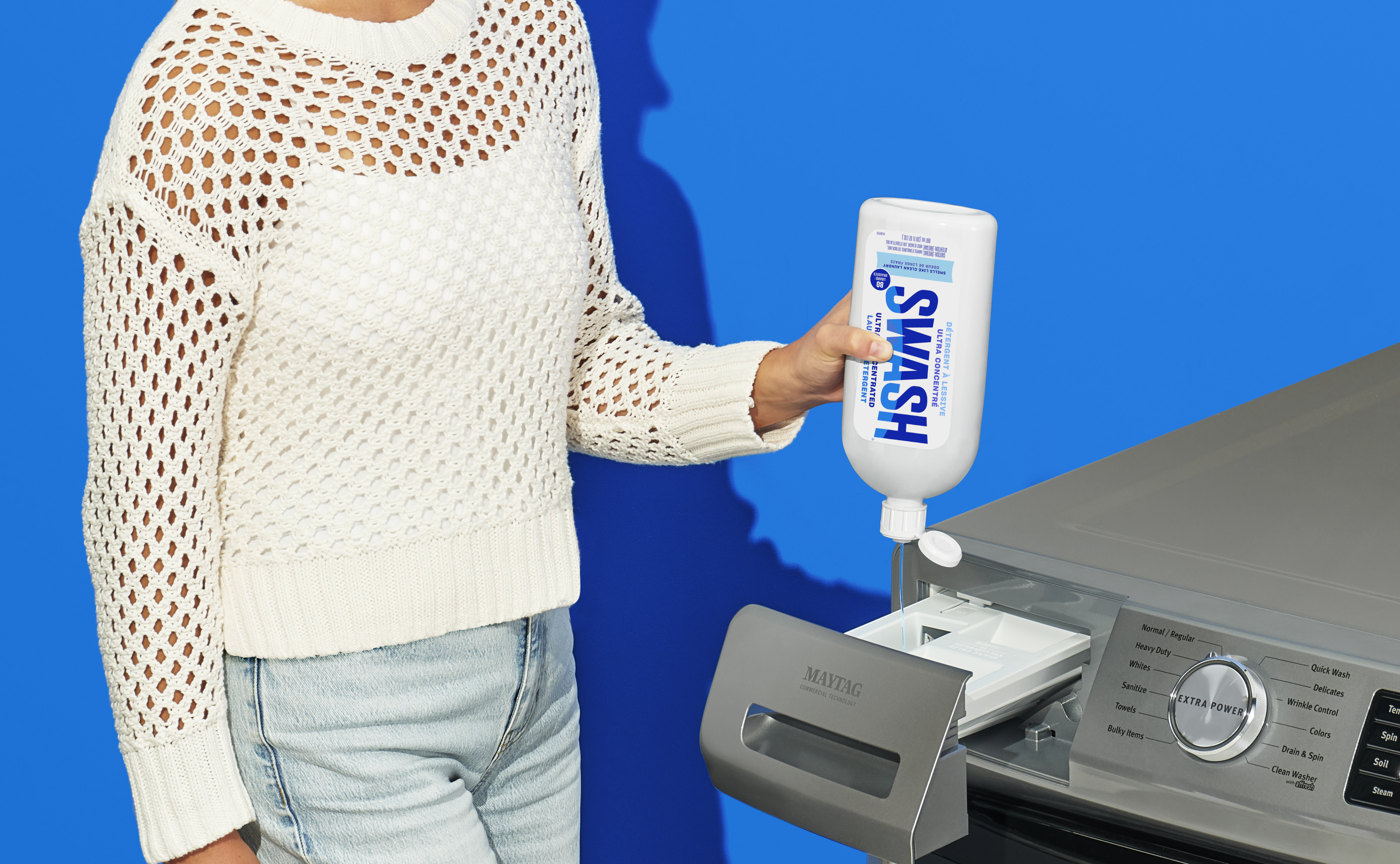 Une image sur sur fond bleu d'une personne qui verse du détergent d'une bouteille de Swash dans le distributeur de détergent d'une laveuse Maytag. 