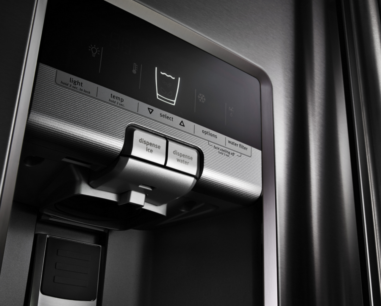 Dramatic, close-up shot of a black Maytag refrigerator ice and water dispenser. Dramatic, close-up shot of a black Maytag refrigerator ice and water dispenser.