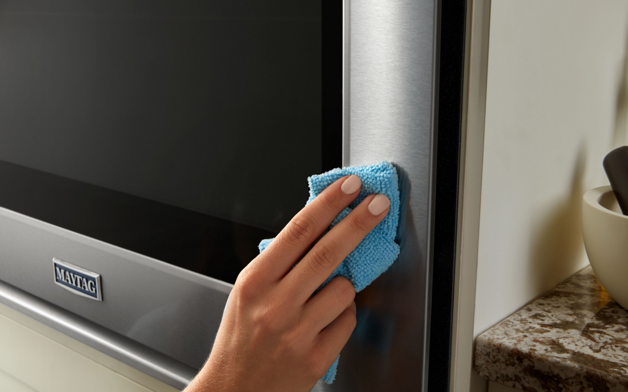 A person wipes down the stainless steel exterior of a Maytag oven.