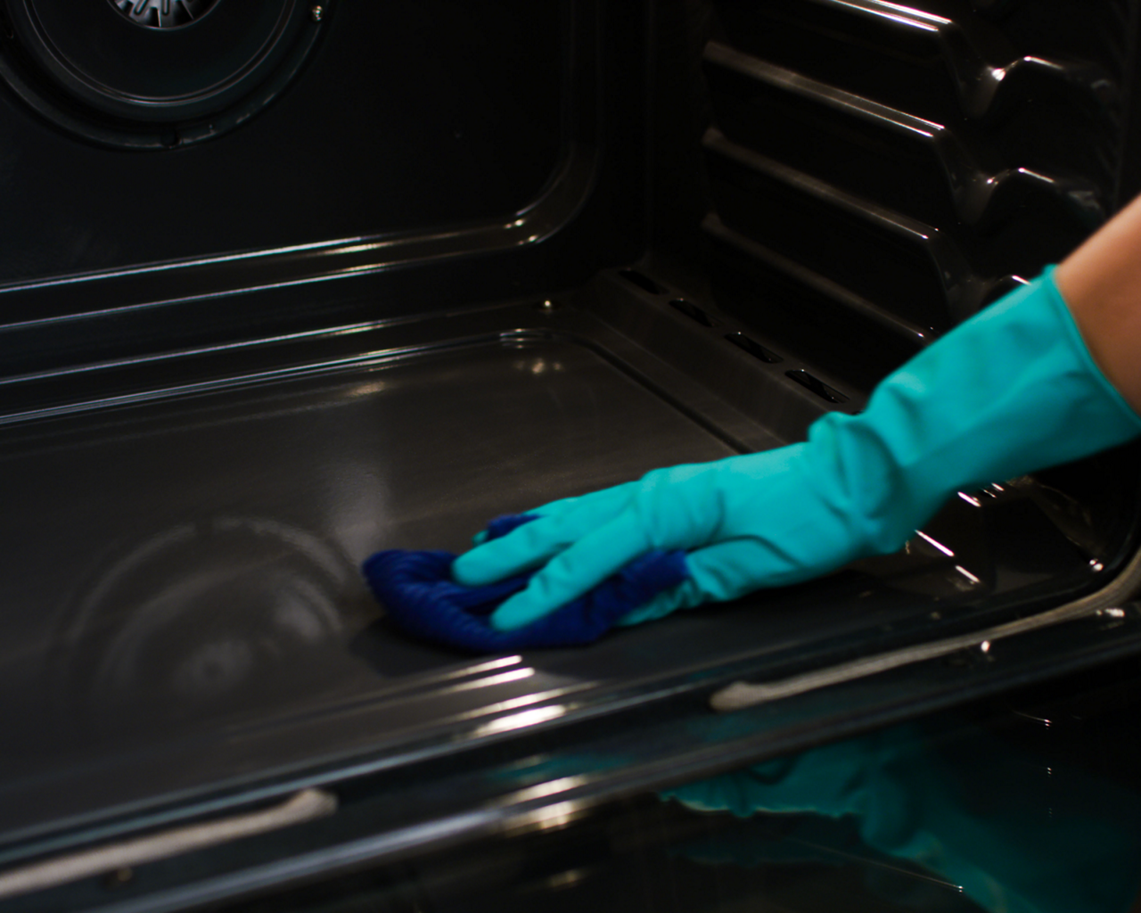 A person wipes down the bottom of an oven.