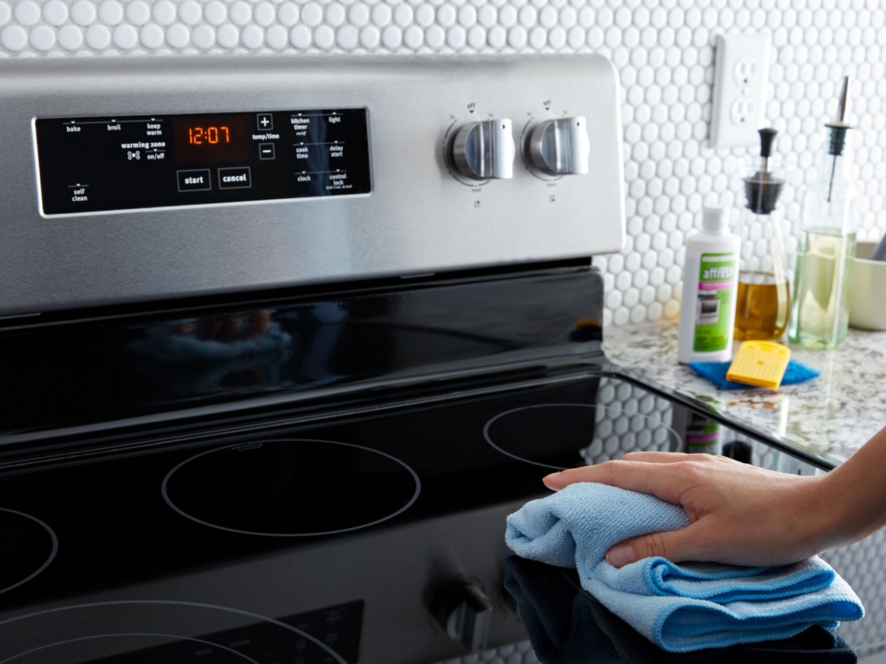 A person wipes down the glass cooktop of a Maytag range.