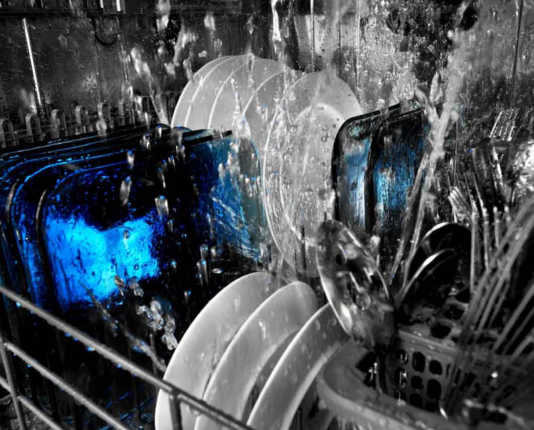 An inside view of a dishwasher cleaning a load of dishes and silverware.