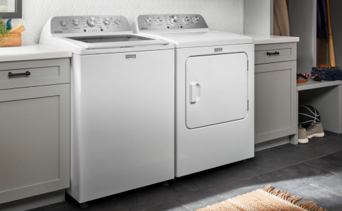 White Maytag® top load washer and front load dryer side by side in a laundry room next to shelves