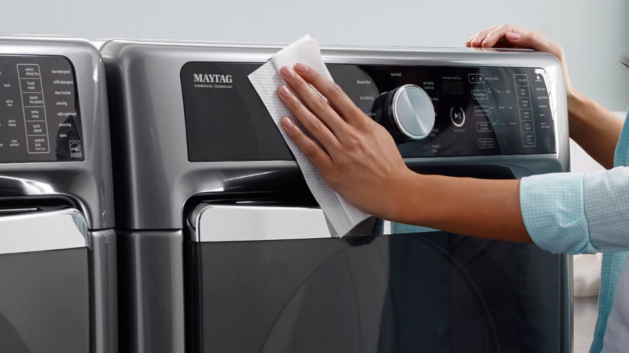 A woman cleaning the outside of a Maytag ® front-load washer.