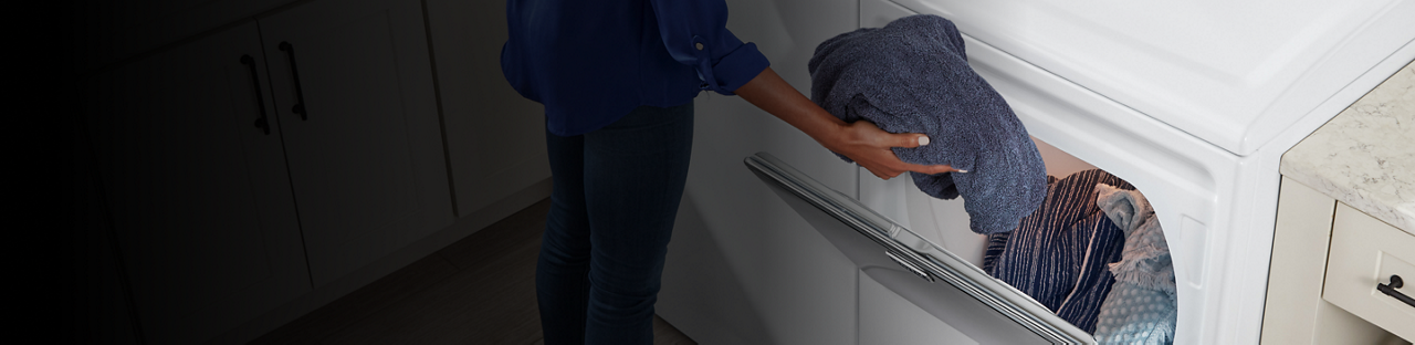 A woman puts towels in a dryer.