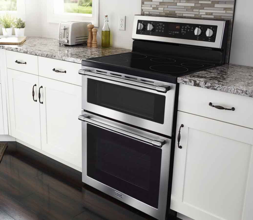 Une cuisinière électrique en acier inoxydable avec un four double dans une cuisine moderne et blanche.