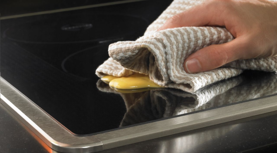 Une personne essuyant la surface d'une table de cuisson à induction avec un chiffon. 
