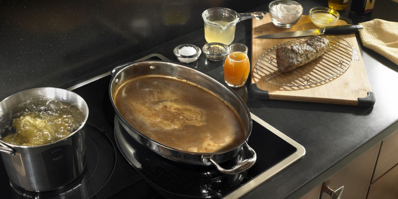 Pots and pans sit on an induction cooktop next to ingredients and cooking equipment on a countertop.