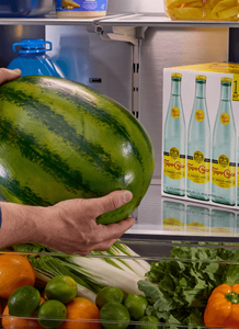 A person placing a watermelon inside a Maytag® refrigerator