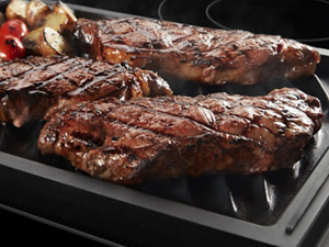 Three grilled steaks and vegetables on a grill pan