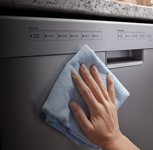 Person wiping down the door panel of a stainless steel dishwasher