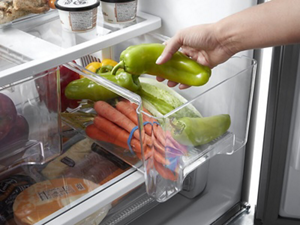 A hand removing produce from an open crisper drawer