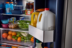 Open refrigerator door with milk and juice in gallon door bins