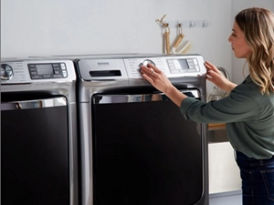  A woman turns the knob on a Maytag laundry appliance, which is next to another Maytag laundry appliance.